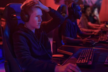 Kulaklıklı sinirli genç adam bilgisayarın önünde oturuyor ve maçı kaybederken saçlarını tutuyor.