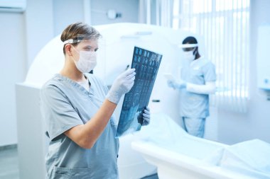 Güvenlik kalkanında odaklanmış radyoloji uzmanı hastanede CT tarayıcısına karşı beyin röntgeni görüntüsüyle çalışıyor.