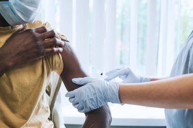 Hastanede ikiyüzlü aşılar yaptırırken elinde tişört olan tanınmamış siyahi bir adamın yakın çekimi.