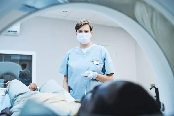 stock image Female radiologist in mask and gloves pushing button on control panel while providing diagnostic imaging of patient