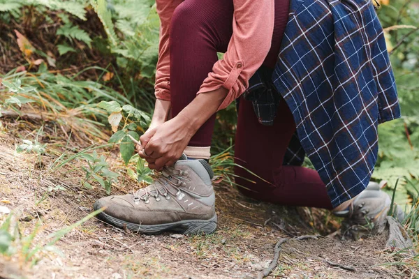 穿着栗色腿的无法辨认的女人单膝站立并在远足时系鞋带的特写 — 图库照片