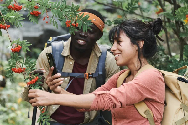 一对快乐的年轻多种族的徒步旅行者 背着背包在森林里给树莓拍照 — 图库照片