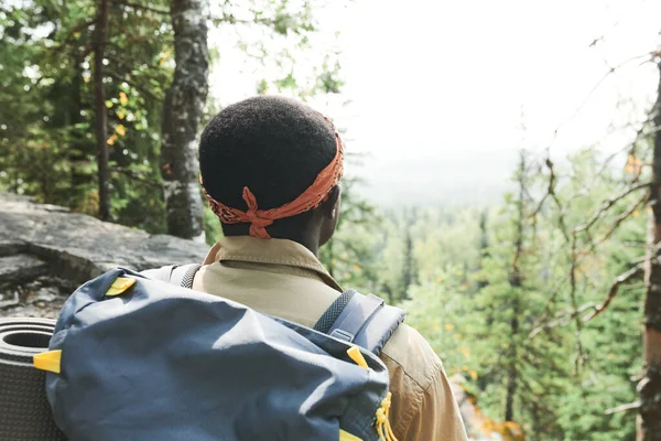 带头巾的黑色背包客站在山上望着森林的后视镜 — 图库照片