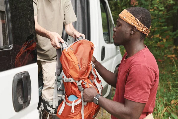 不明身份的徒步旅行者把背包送给身穿橙色头巾的黑人男子 而他们却把面包车靠在森林里 — 图库照片