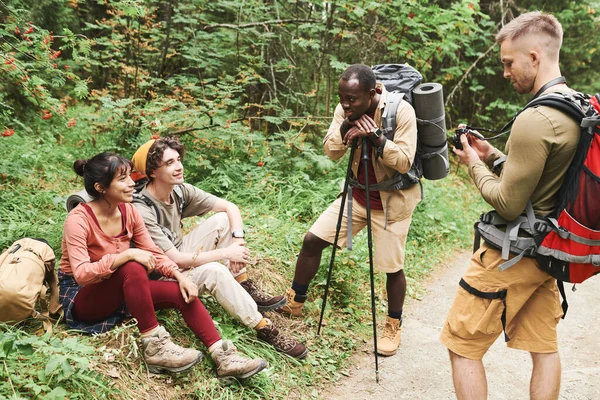 正の若い多民族ハイカーのグループとバックパック草の上に残り 森の中で一緒にチャット — ストック写真