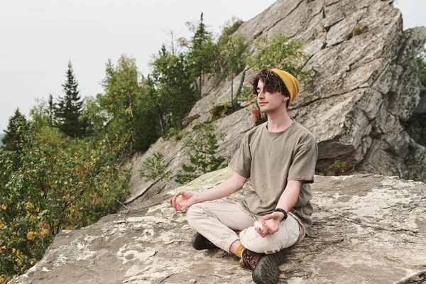 心满意足的年轻白种人头戴礼帽 坐着荷花的姿势 坐在外面的大石头上沉思 — 图库照片