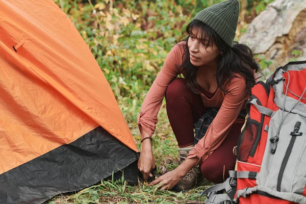 年轻的混血女子戴着帽子在森林里搭起橙色帐篷 准备露营 — 图库照片