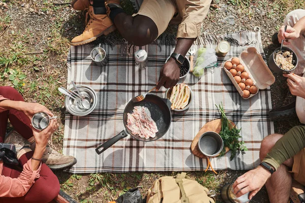 stock image Directly above view of unrecognizable hikers sitting on ground and frying bacon on pan at camping