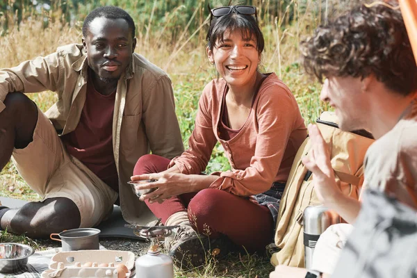 一群兴奋的年轻多民族朋友坐在草地上 一边吃着食物一边在森林远足 — 图库照片