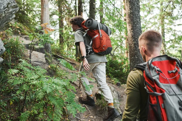 山の中をハイキングしながら急な崖を登るバックパックを持つ若い男性の背面ビュー — ストック写真