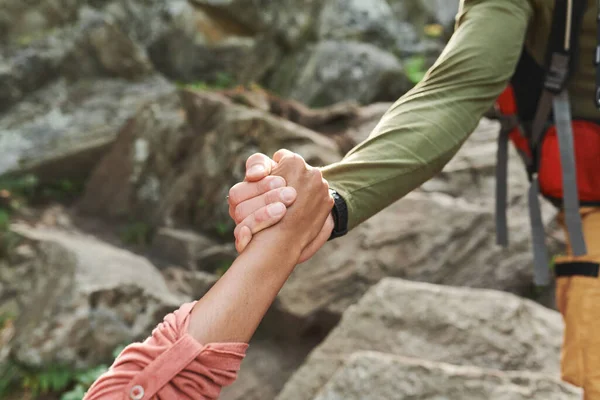 Close-up of unrecognizable man pulling hand of female hiker while helping her to move up stone