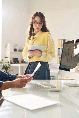 Genç iş kadını ofisinde dikilirken dijital tablet kullanıyor.