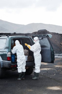 Terk edilmiş bölgede kurtarma arabasının başında duran kara bilim adamları tehlikeli madde kıyafetlerini, maskeleri ve eldivenleri giydirdiler.