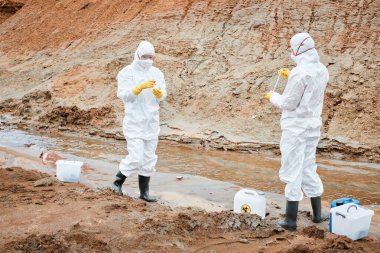 Maskeli, eldivenli ve koruyucu elbiseli çevre bilimcileri zehirli maddelerle çalışıyor.