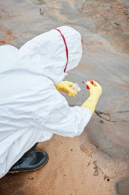 Sarı eldivenli tanınmayan bir çevre araştırmacısı kirli suda oturuyor ve toprak örneğini konteynıra koyuyor.