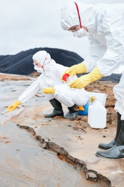 Koruyucu giysiler ve solunum cihazları içindeki çevre bilimcileri zehirli alandaki kirlenmiş örnekleri araştırırken numuneleri konteynırlara koyuyorlar.