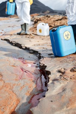 Zehirli işaretleri olan plastik kaplar kırmızı sıvıyla kurumuş nehrin yakınındaki kirli araziye yerleştirilmiş.