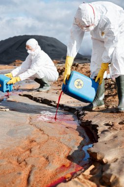 Biyolojik tehlike giysileri ve maskeli bilim adamları kirli suya zehirli sıvı ekliyorlar.