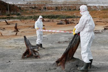 Koruyucu giysi ve maskeli ekologlar kirlilik bölgesini kapatırken barikat bandı kullanıyorlar
