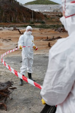 Çevre uzmanları, kirlenmiş bölgeyi uyarı kurdelesiyle işaretleyerek terk edilmiş bölgelerde koruyucu giysiler giyiyorlar.