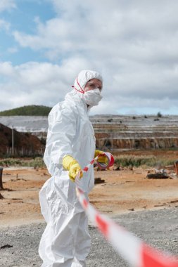 Kirlilik uzmanı maske ve koruyucu giysi tehlikeli bölgeleri kırmızı ve beyaz bantla işaretliyor.