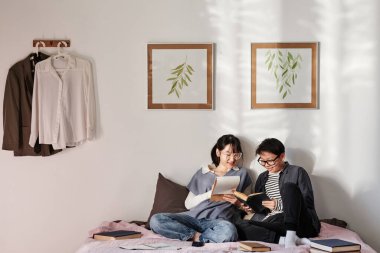 Sınava hazırlanırken birbirine destek olan gülümseyen Asyalı çift duvarında resimlerle öğrenci odasında.