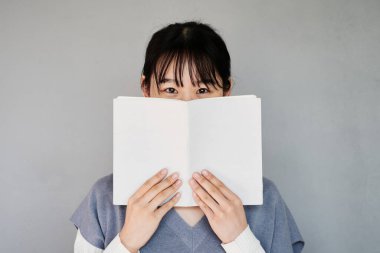 Asyalı öğrenci portresi. Yüzü kitapların arkasına gizlenmiş kâküllü.