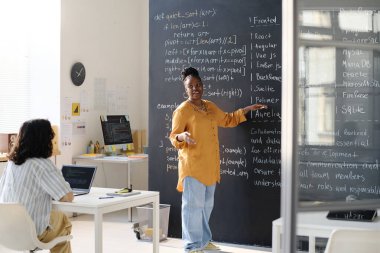 Afro-Amerikan öğretmen tahtaya bilgi veriyor ve öğrencilere bilgi işlem öğretiyor.