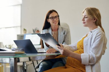 Sosyal hizmetler görevlisiyle görüşürken genç hamile bir kadın belge okuyor.