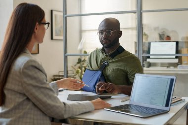 Yaralanan Afrikalı Amerikalı bir adam sigorta acentasıyla ofisinde toplantı yapıyor.