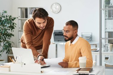 Orta Doğulu yönetici, modern ofisteki meslektaşlarıyla birlikte verileri incelerken kağıdı kontrol ediyor.