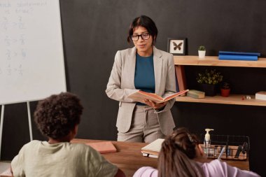 İspanyolca öğretmeni elinde kitapla sınıftaki çocuklarla konuşuyor.