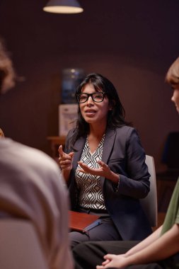 Modern psikoterapistin depresyonda olan bir grup insanla bir şeyler tartıştığı dikey bir fotoğraf.