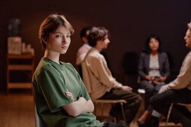 Kollarını kavuşturup kameraya bakarken grup psikoterapisine katılan genç bir kadının yatay görüntüsü.