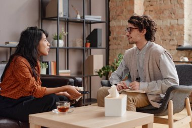 Profesyonel psikoloğun önünde oturan genç bir kadının başarılı anları anlattığı yatay bir fotoğraf.