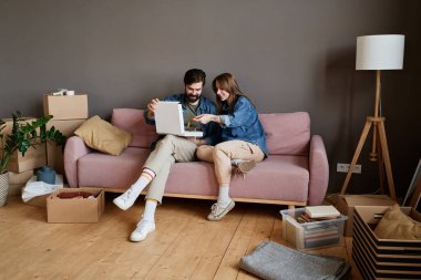 Genç adam ve kadın, yeni eve taşındıktan sonra kanepede birlikte pizza yiyorlar.