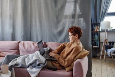 Yetişkin, beyaz bir kadının evde dizüstü bilgisayarla çalışırken grip olmasının yatay yan görüntüsü.