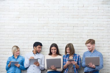 Neşeli arkadaşlar dizüstü bilgisayarda komik videolar izleyip aletlerinin yardımıyla interneti karıştırırken arka planda beyaz tuğla bir duvar görüyorlar.