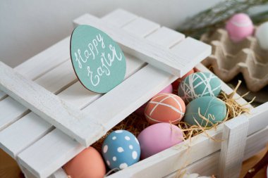 Paskalya dekoru: samandaki boyalı yumurtalarla dolu kapağı açık beyaz tahta kutunun yakın çekimi, Mutlu Paskalyalar kartı