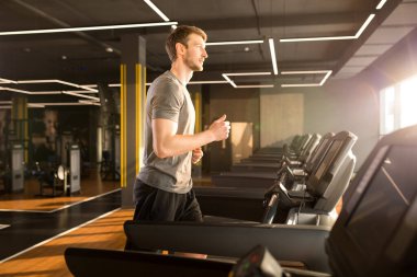Spor kıyafetli genç adam spor salonunda pencerenin önünde koşu bandında koşuyor.