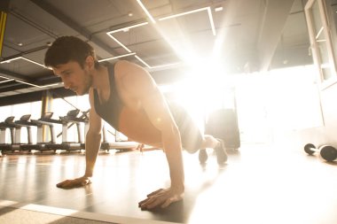 Spor kıyafetli genç kaslı adam spor salonunda antrenman yaparken yerden şınav çekiyor.