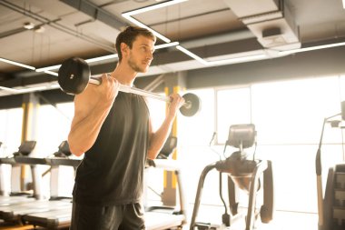 Genç sporcu tişörtünü giyiyor ve spor salonunda halterle egzersiz yapıyor.
