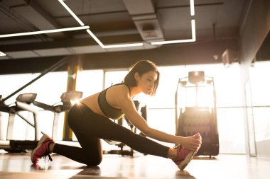 Spor kıyafetleri içinde sağlıklı, zayıf bir kadın sağlık kulübündeki spor eğitimi sırasında bacağını esnetiyor.