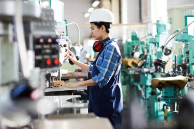 Ciddi genç kadın mühendis sanayi makinesinin kontrol panelinin kontrol düğmesine basarak üretim sürecine odaklandı