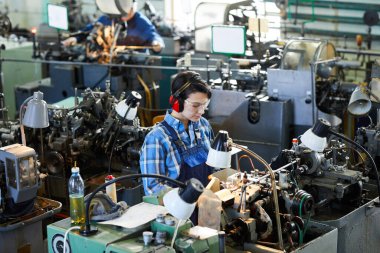 Torna makinesiyle tezgahta duran ve küçük parçaları işlemekle meşgul genç bir çocuk gibi görünen ciddi meşgul bir kız.