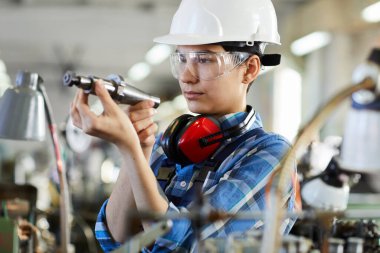 İnşaat başlığı ve güvenlik gözlüğü yapımında ciddi kadın teknik mühendis saat hareketleri üretmek için makineyi tamir ederken matkap ucunu kontrol ediyor