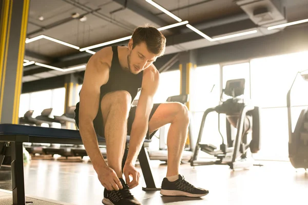 Young man in sports clothing sitting on bench in sport club and preparing for his training