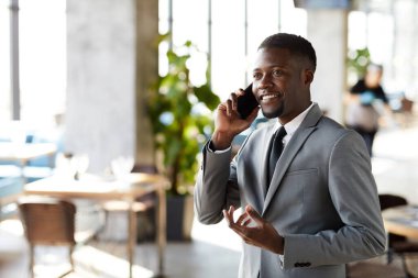 Kendine güvenen, sakallı, iş merkezinin lobisinde duran ve cep telefonuyla konuşurken el kol hareketi yapan genç bir siyah menajer.