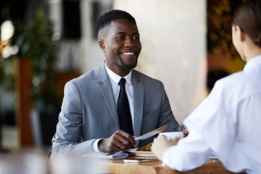 Gülümseyen genç afro-amerikan iş adamı masada oturup salata yerken iş yemeğinden bahsediyordu.