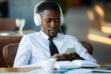 Masasında ayılar oturan ve kulaklıkla müzik dinlerken mesaj atan konsantre olmuş genç zenci işadamı kafede dinleniyor.